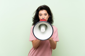 Young woman over isolated green background shouting through a megaphone