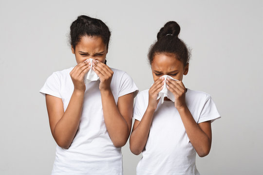 Two young girls blowing noses over grey background