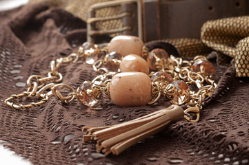 soft focus of chain with pink beads near lace belt and golgen cloth on brown textile lace