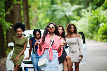 Group of five happy african american girls posed against car, one of them show keys.