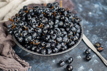 Large, black, wine grapes. It is covered with a white coating called yeast. With the help of them, wine is obtained. Drops of water on the berries, next to a gray fabric for decoration. 