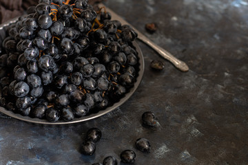 Large, black, wine grapes. It is covered with a white coating called yeast. With the help of them, wine is obtained. Drops of water on the berries, next to a gray fabric for decoration. 