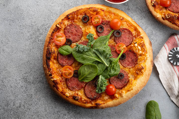 Tasty pepperoni pizza and cooking ingredients tomatoes basil on grey concrete background. Top view of hot pepperoni pizza. With copy space for text.