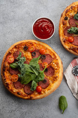 Tasty pepperoni pizza and cooking ingredients tomatoes basil on grey concrete background. Top view of hot pepperoni pizza. With copy space for text.
