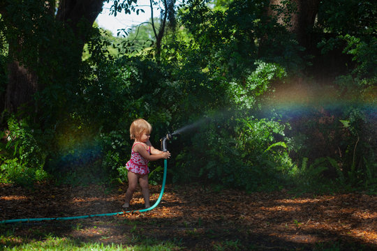 A little girl playing with a hose making rainbows with a hose