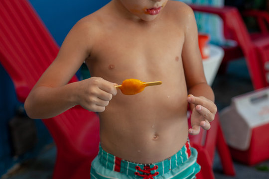 A little boy in a swimsuit  having popsicle as a snack outside
