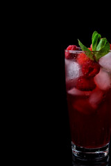 Red drink with ice, raspberries and mint in a tall glass against the black background
