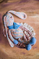 A knitted rabbit in pastel colors sits in a basket with vines.