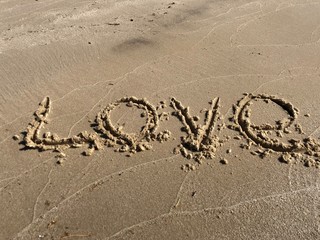 The inscription "Love" on the sandy shore. Sign drawn on the sand, closeup. Concept: declaration of love.