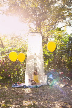 Two little girls playing outside and reading books in the yard in a shade tent with balloons