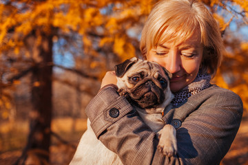 Woman walking pug dog in autumn park. Happy lady hugging pet. Best friends