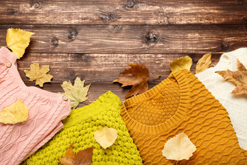 Woolen sweaters with autumn leafs on brown wooden table