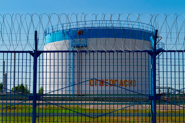 A huge tank of petroleum products at the factory behind a fence with barbed wire. The inscription in Russian is "Flammable." Front view.
