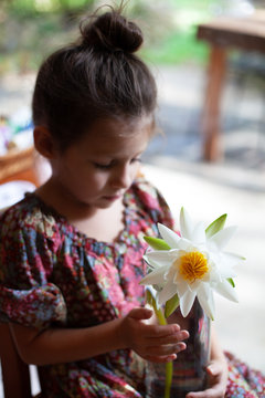 A little girl with her hair in a bun, putting a lotus flower into a vase