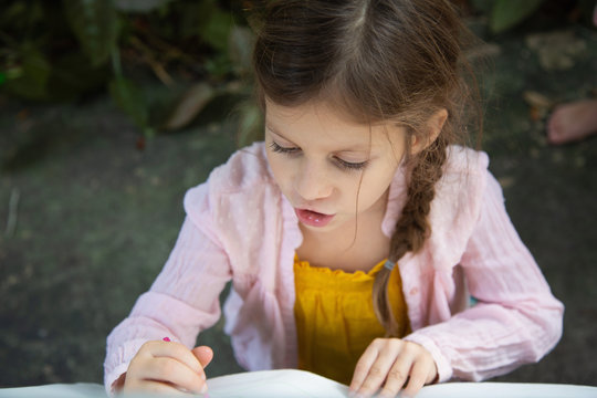 A little girl reading a story from a book outside