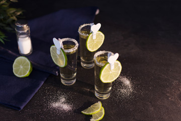 Shot glasses of gold tequila with a rim of salt, and lime slices.