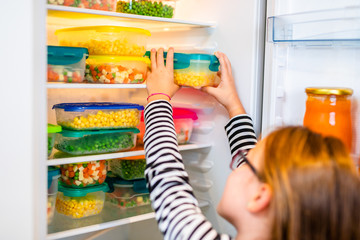 Beautiful and happy little girl working in home kitchen and preparing vegetables for winter in vacuum containers.