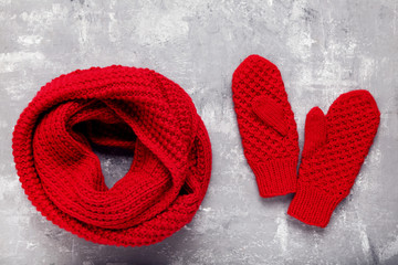 Knitted red scarf and pair of gloves on grey background