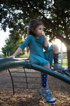 A little girl sitting atop a jungle gym outside at a playground