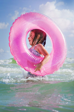 Girl playing in waves with pink beach float