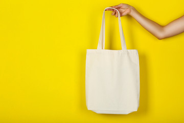Female hand holding white cotton eco bag on yellow background