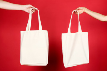 Female hands holding white cotton eco bags on red background