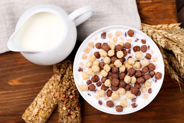 Corn flakes in bowl with milk and granola bars on brown wooden table