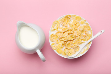 Corn flakes in bowl with milk and spoon on pink background