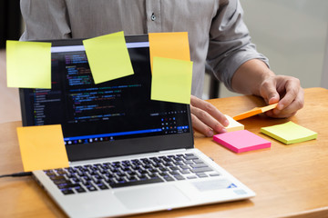 Tasks on sticky note cards on laptop computer with source code program of business software...