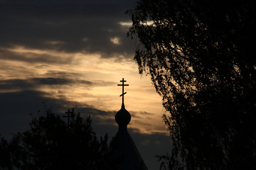 Cross on the dome of the Orthodox Church against the background of a bright sky among dark clouds