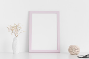 Pink frame mockup with workspace accessories  and gypshophila in a vase on a white table.Portrait orientation.
