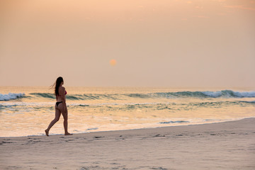 Fototapeta na wymiar Beautiful model walking in a bikini on the beach during sunset.