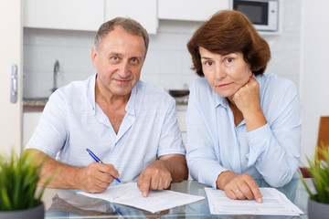 Fototapeta premium Smiling mature couple at table in home kitchen filling up documents