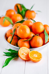 Tangerines (oranges, clementines, citrus fruits) with green leaves over wooden background with copy space.bowl of fresh mandarins