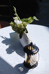 white gladiolus in a decorative vase and a portable lantern on a white table