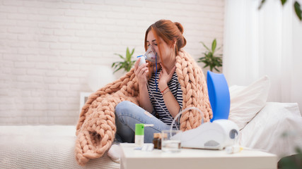 Young woman doing inhalation with a nebulizer at home - obrazy, fototapety, plakaty