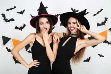 Two young women in black halloween costumes with paper bats and flags on white background