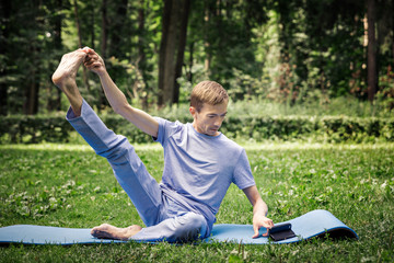 Young attractive white man learns to meditate in the park in front of a smartphone.