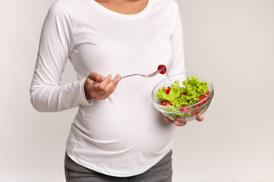 Unrecognizable Pregnant Woman Eating Salad Standing Over White Background