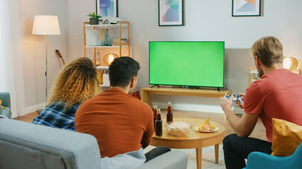 In the Living Room Three Friends Competitively Play Video Games on Green Chroma Key Screen, Using...