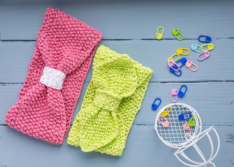 Two knitted headbands for girls: light green, pink. Hair bands are on a blue wooden background. Texture for knitting and place for signature and small decorative cage. 