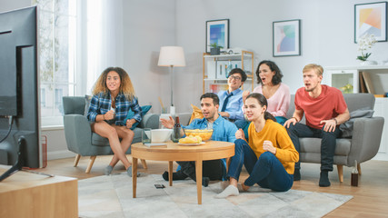 Fototapeta na wymiar At Home Diverse Group Friends Watching TV Together, Eating Snacks and Drinking Beverage. They Probably Watching Sports Game or Fun Movie.