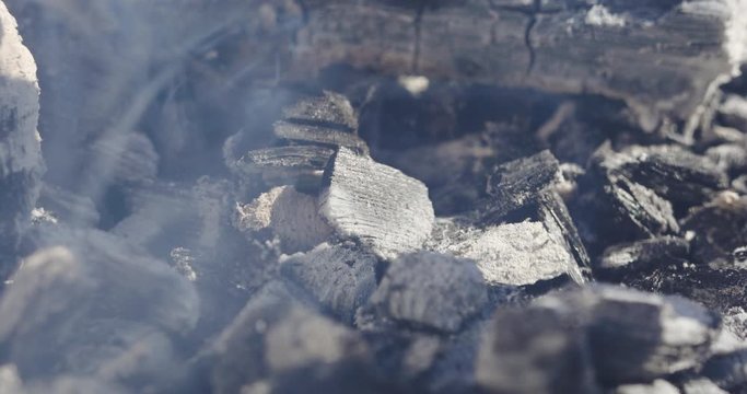 black and grey coal pieces fester creating small white smoke clouds over barbecue grill extreme close view