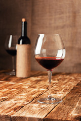 A glass of red wine next to a bottle in burlap on a wooden table in the cellar of the winery.