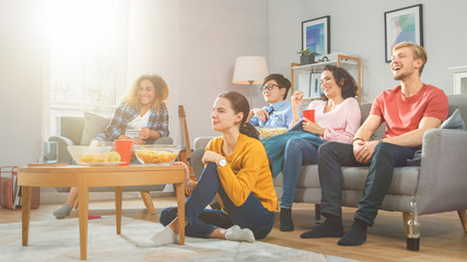 At Home Diverse Group Friends Watching TV Together, Eating Snacks and Drinking Beverage. They Probably Watching Sports Game, Movie or Sitcom TV Show. Young People Having Fun Together.