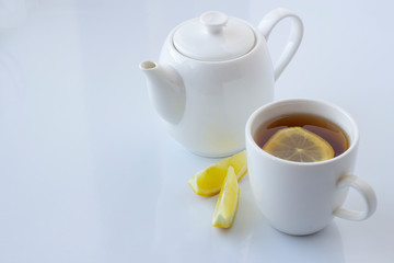 Tea with lemon in a white cup and a white teapot on a white background