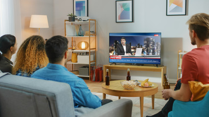 Obraz premium Happy Friends Sitting At Home Watching News. Relaxing on a Couch.right Cozy Apartment with Friends Eating Snacks and Having Fun.