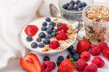 White yogurt in bowl with oatmeal and strawberries, blueberries and raspberries on the top.