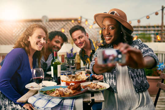 Group of diverse friends taking selfies pictures having dinner al fresco in urban setting
