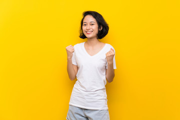 Asian young woman over isolated yellow wall celebrating a victory in winner position